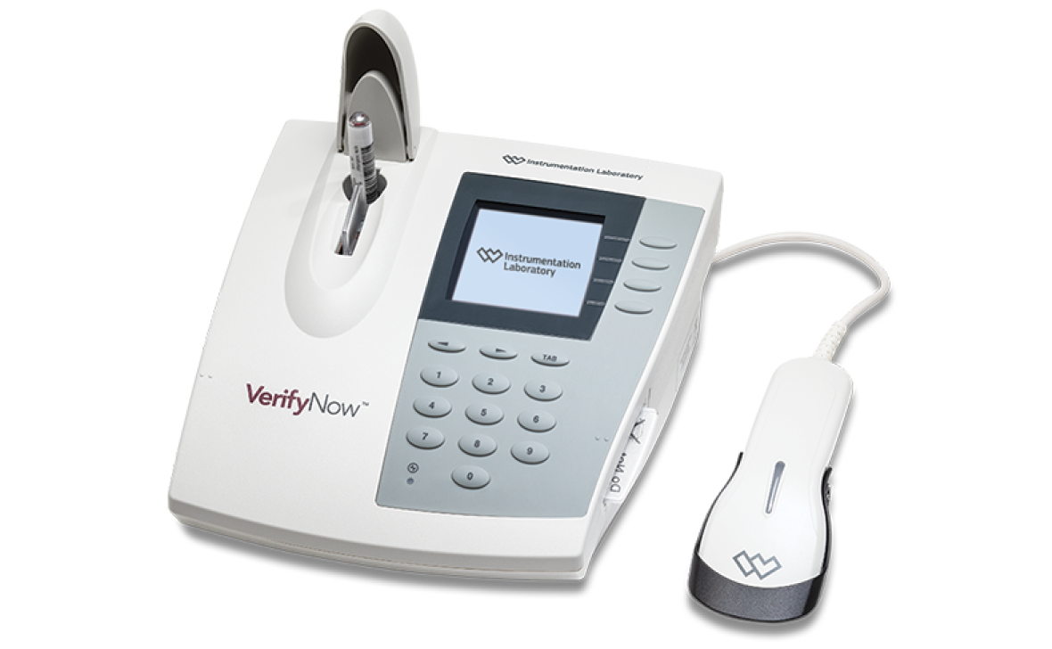 A white VerifyNow medical diagnostic device, featuring a digital screen, a numeric keypad, a test cartridge slot with a sample inserted, and a connected handheld barcode scanner.